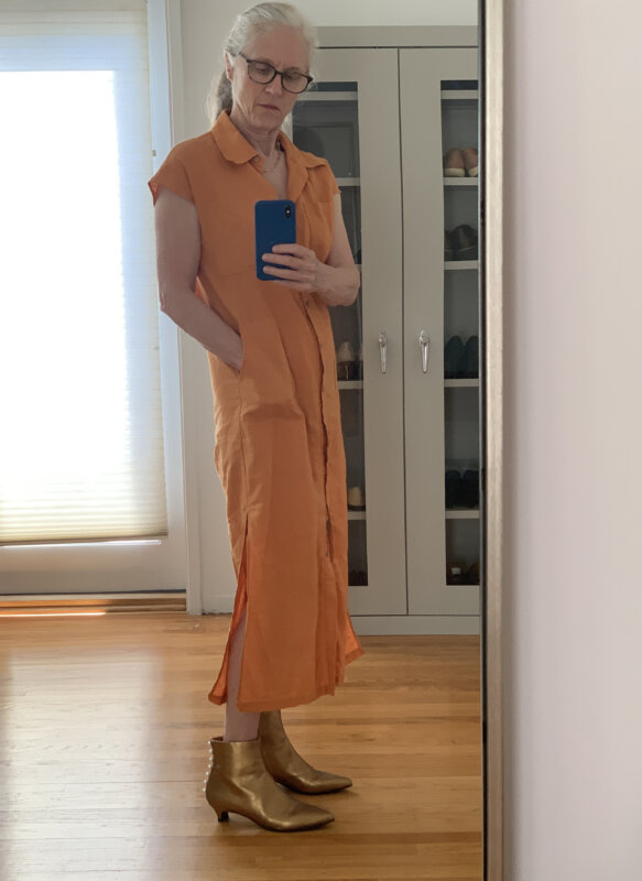 Orange linen dress and gold booties worn by woman with white hair.