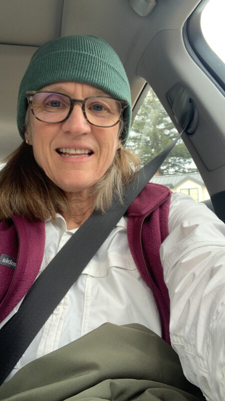 A middle-aged woman in a green beanie and outdoor gear