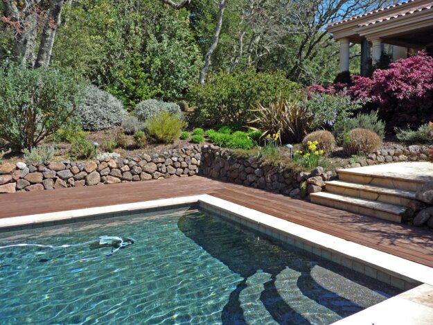 Black bottom swimming pool full of water, with steps and a hillside garden