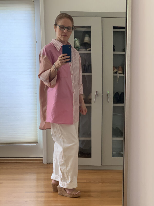 Older woman wearing oversized pink striped shirt, white jeans, and platform sandals