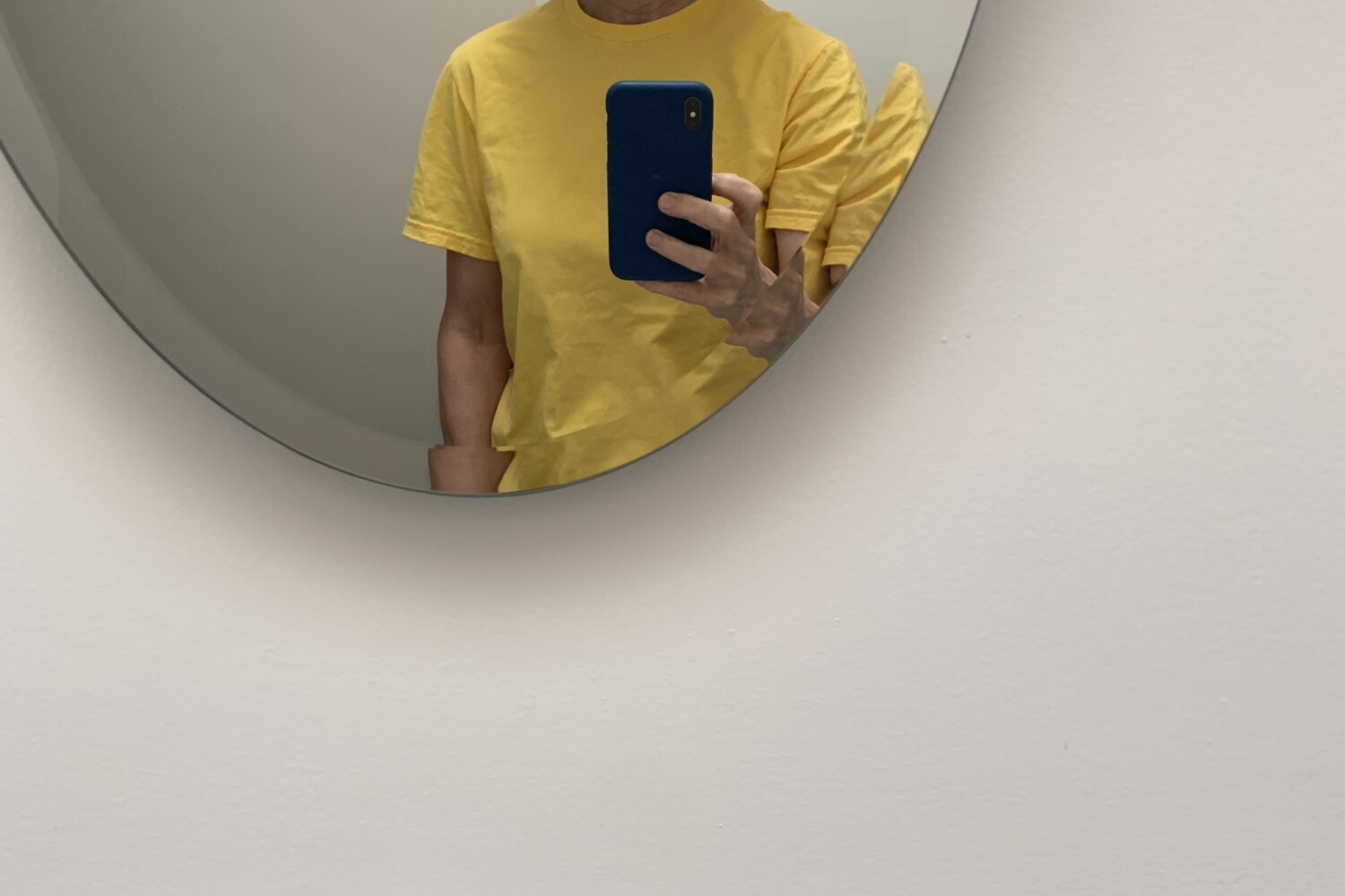 Woman wearing Tilley hat, Ray-Bans and a yellow shirt, looking in mirror