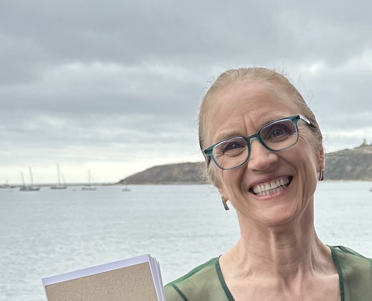 Woman in her 60s smiling broadly in front of Pillar Point Harbor.