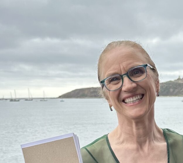 Woman in her 60s smiling broadly in front of Pillar Point Harbor.