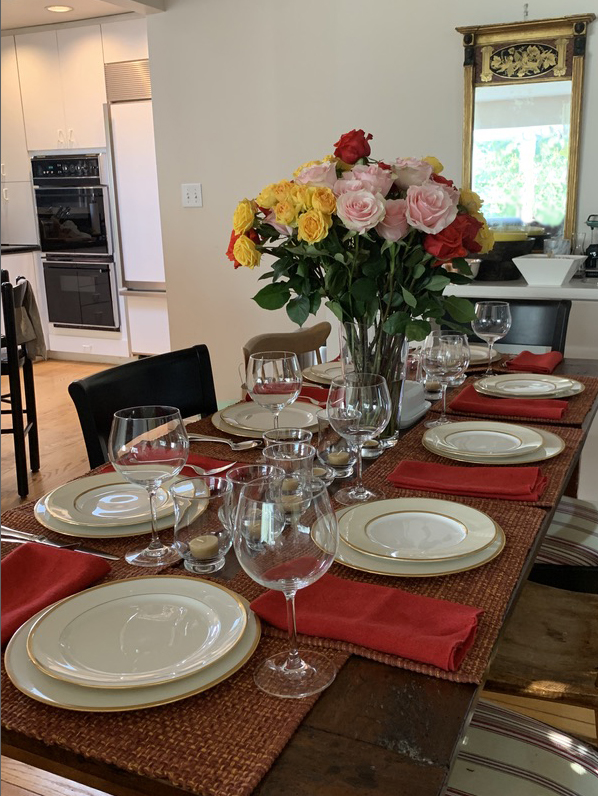 A table mostly set for Thanksgiving, with a centerpiece of pink and red and yellow roses.
