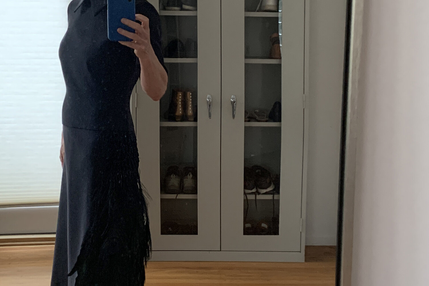 An older woman modeling a black silk faille dress with a peacock feather and beads ornament at the hip.