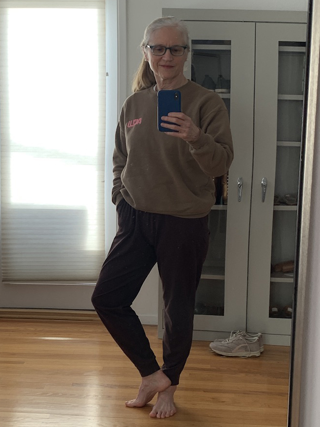 Older woman wearing a brown ACLU-embroidered sweatshirt and standing on one foot